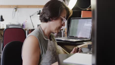 trabajadora caucásica ocupada con una computadora portátil modelando joyas en el estudio en cámara lenta