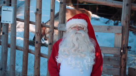 santa está de pie junto a una valla de madera y hablando con la cámara