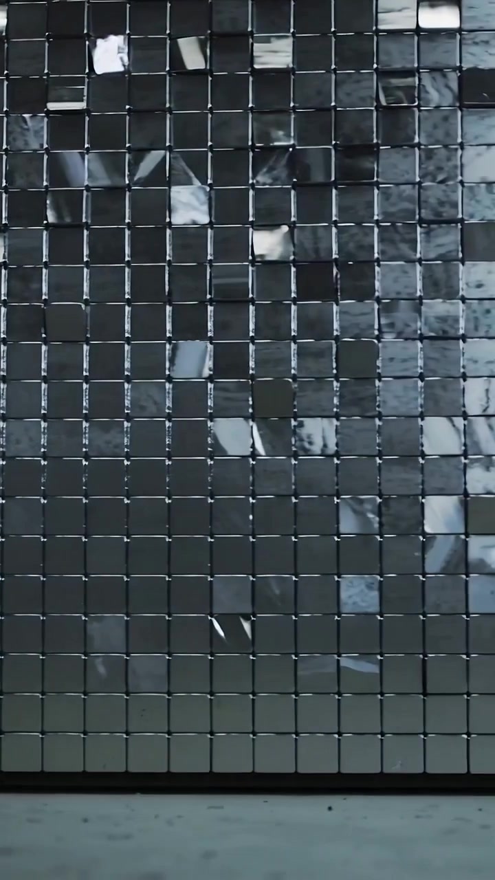 Vídeo vertical: Câmera deslizando revelando cubo com azulejos brilhantes, mostrando reflexos ondulados em galeria.