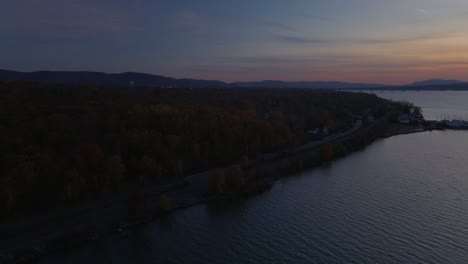 aerial side pan of the hudson river just after sundown with autumn forests, a boatyard, and mountains in the distance