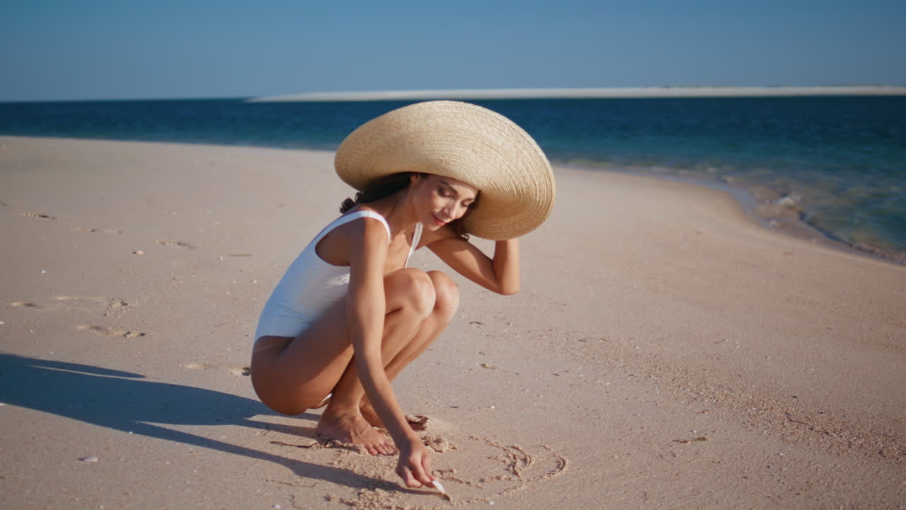 Woman drawing ocean sand enjoying summer vacation on resort. Smiling brunette