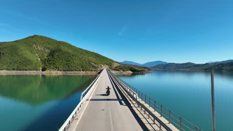 motorcycle riding over a bridge crossing a blue lake