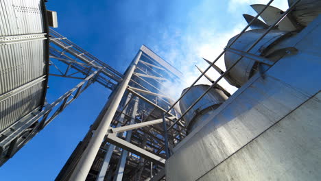 exterior of agricultural plant. smoke going up from industry during drying and processing grain. view from below.
