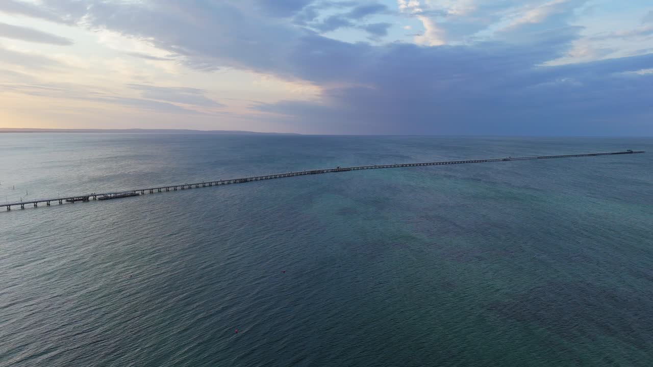 Drone flying over Busselton Jetty at sunset as train goes along the timber pier