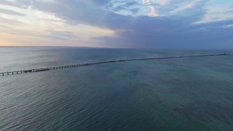 drone flying over busselton jetty at sunset as train goes along the timber pier