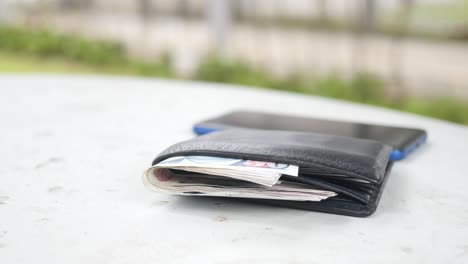 billetera de cuero negra con dinero en efectivo y teléfono móvil en una mesa al aire libre