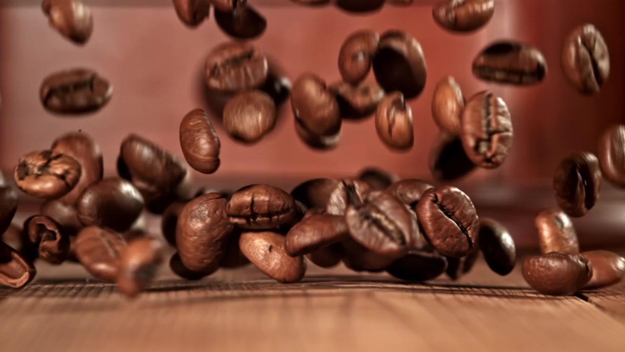 Ristede kaffebønner falder i slowmotion ned på en træoverflade