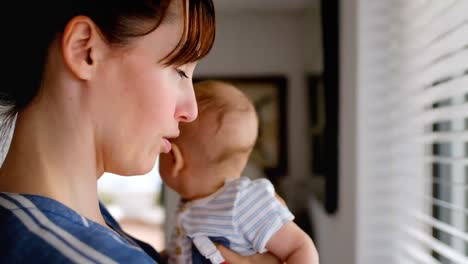 mamá joven de pie cerca de la ventana mientras sostiene al bebé 4k