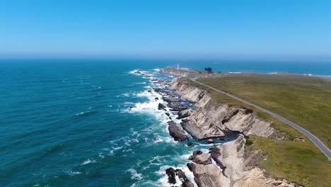 aerial video of a rocky beach coast with a road on the right side along with a blue ocean