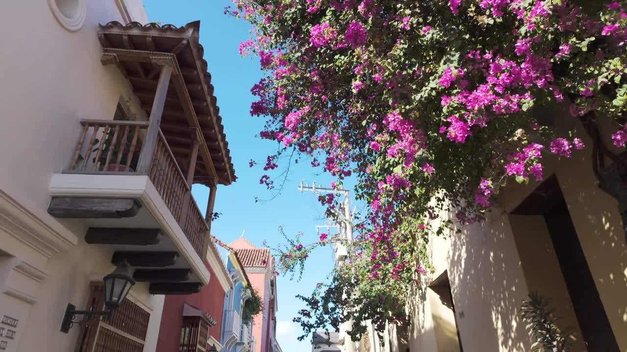 POV: Caminhando por uma rua do centro histórico em Cartagena, Colômbia, passando por um edifício com plantas coloridas penduradas no telhado.