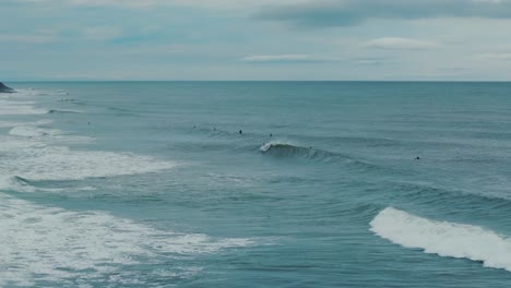 grandes olas chocando contra la playa con surfistas en el agua, día de verano