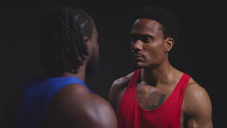 Close-Up-Of-Two-Male-Boxers-Going-Face-To-Face-Before-Boxing-Match-Staring-At-Opponent-Against-Black-Background