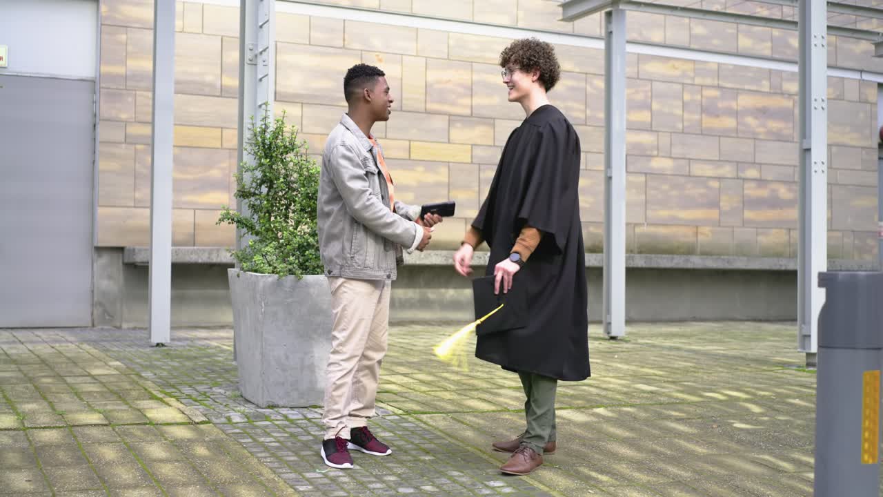 Diverse male friends greeting after approach at campus grad checking phone holding cap celebrating