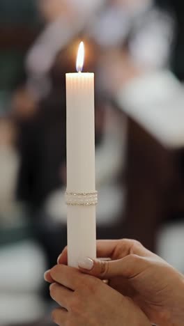 the bride stands in the church at the wedding and holds a lit candle in her hands