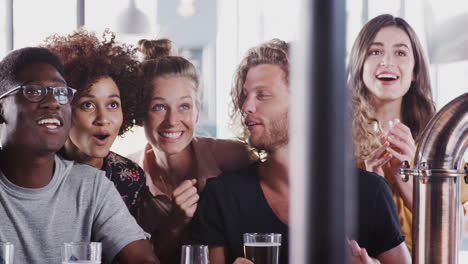 Grupo-De-Amigos-Y-Amigas-Celebrando-Mientras-Ven-El-Juego-En-La-Pantalla-En-El-Bar-Deportivo