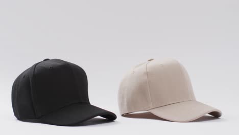 Video-of-black-and-beige-baseball-caps-and-copy-space-on-white-background