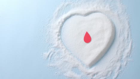 close up of blood drop over sugar in heart shape on blue background, slow motion