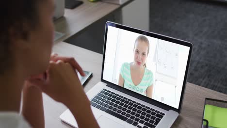 mujer de negocios afroamericana sentada en un escritorio usando una computadora portátil haciendo una videollamada con una colega