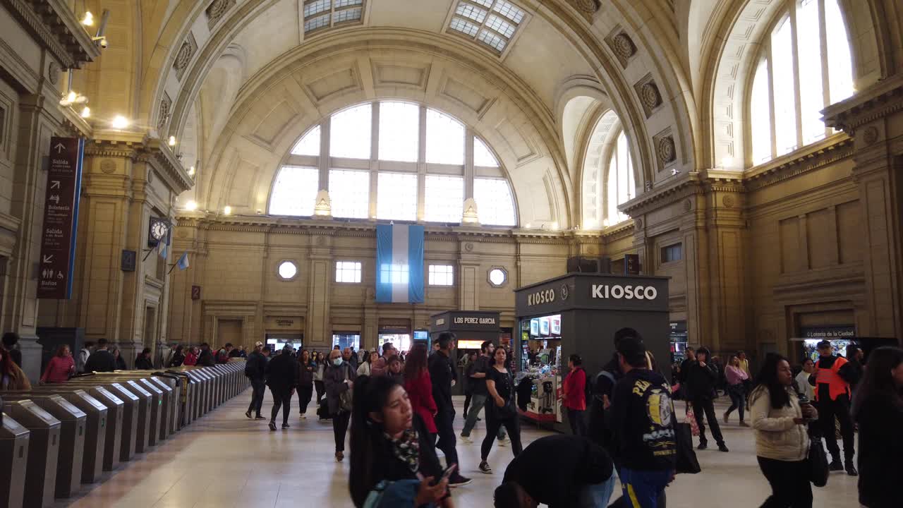 Local Argentine people transit indoors at Constitucion railway station flag and turnstiles in famous landmark