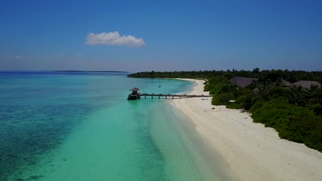 a-horizontal-aerial-view-of-a-resort-hotel-and-its-wood-deck-on-the-turquoise-sea-in-the-Maldives,-drone-footage-on-a-clear-day