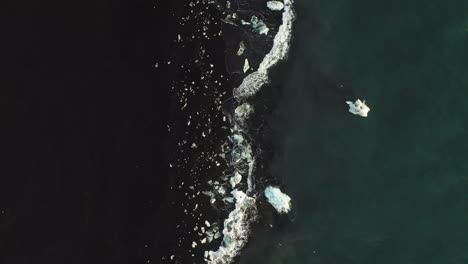 ocean waves splashing on shore of black diamond beach in iceland - aerial top down