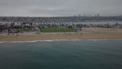 Bewölkter-Strand-Mit-Grasbewachsenem-Park-Und-Palmen-Luftrückzug-über-Dem-Pazifischen-Ozean