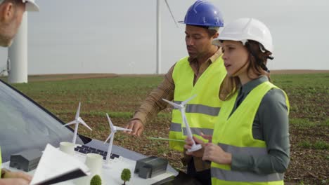 Team-Kaukasischer-Und-Lateinamerikanischer-Ingenieure,-Die-Auf-Dem-Windkraftanlagenfeld-Stehen-Und-über-Das-Projekt-Diskutieren.