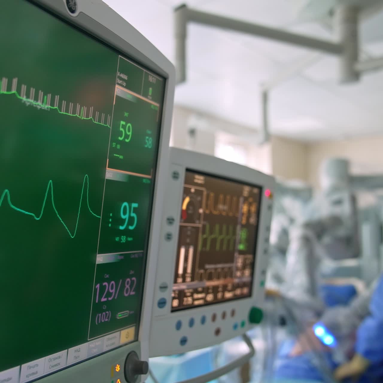 Two screen working at surgery room and showing diverse parameters. Male surgeon performs surgery at backdrop in blur