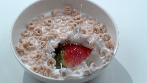 overhead shot of strawberry splashing into bowl of cereal