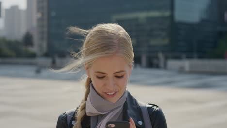 portrait beautiful young blonde woman using smartphone enjoying reading text messages browsing on mobile phone in sunny urban background slow motion