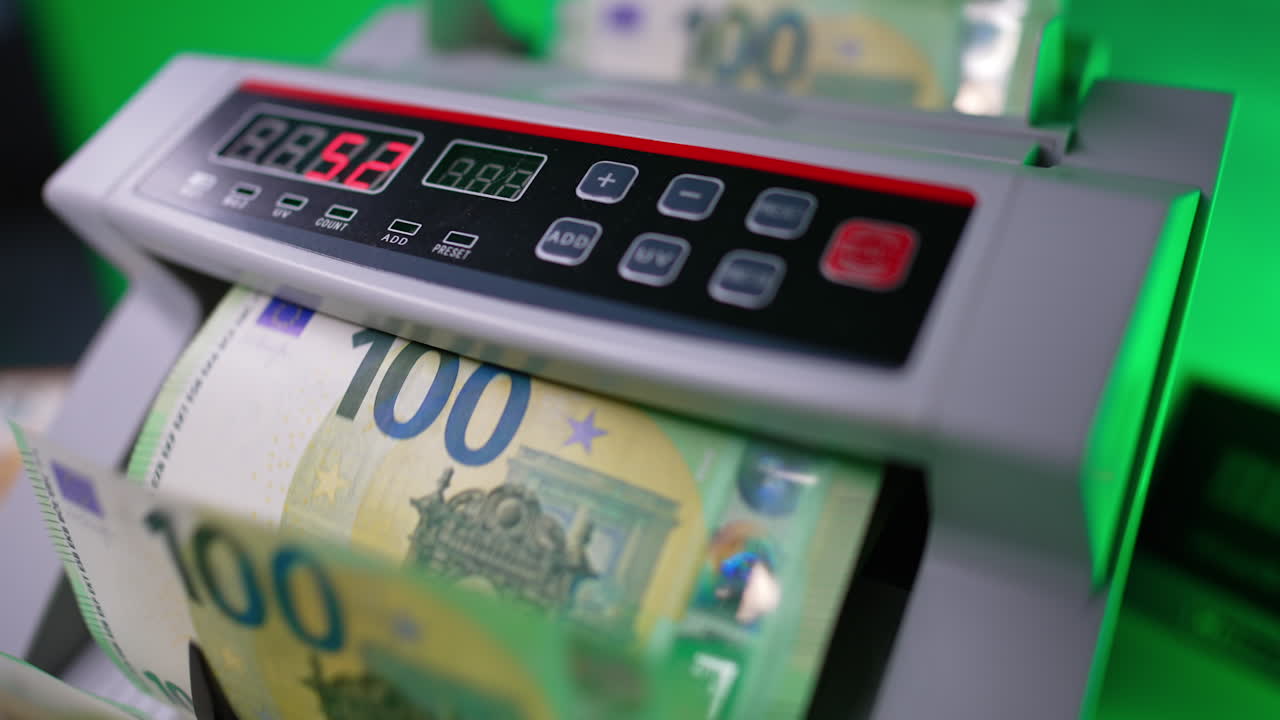 One hundred euro banknotes disappear in cash counting machine. Blades of device quickly rotate the bills. Close up. Blurred backdrop.