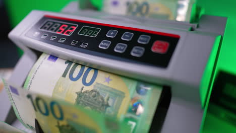 one hundred euro banknotes disappear in cash counting machine. blades of device quickly rotate the bills. close up. blurred backdrop.