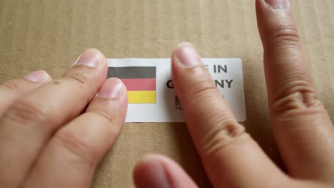 Hände-Bringen-Das-Flaggenetikett-„Made-In-Germany“-Auf-Einem-Versandkarton-Mit-Einem-Barcode-In-Premiumqualität-An