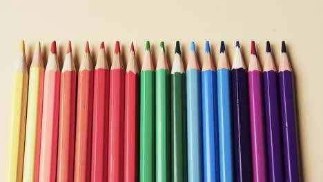 primer plano de lápices de colores dispuestos sobre un fondo beige, en cámara lenta