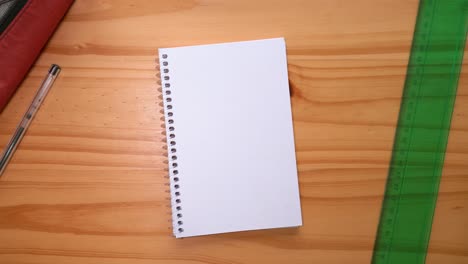 hand places open notebook with blank page on the table with ruler and ballpoint pen on the sides