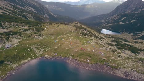 Tilting-shot-revealing-tents-at-the-base-of-a-valley-with-mountains-in-the-background