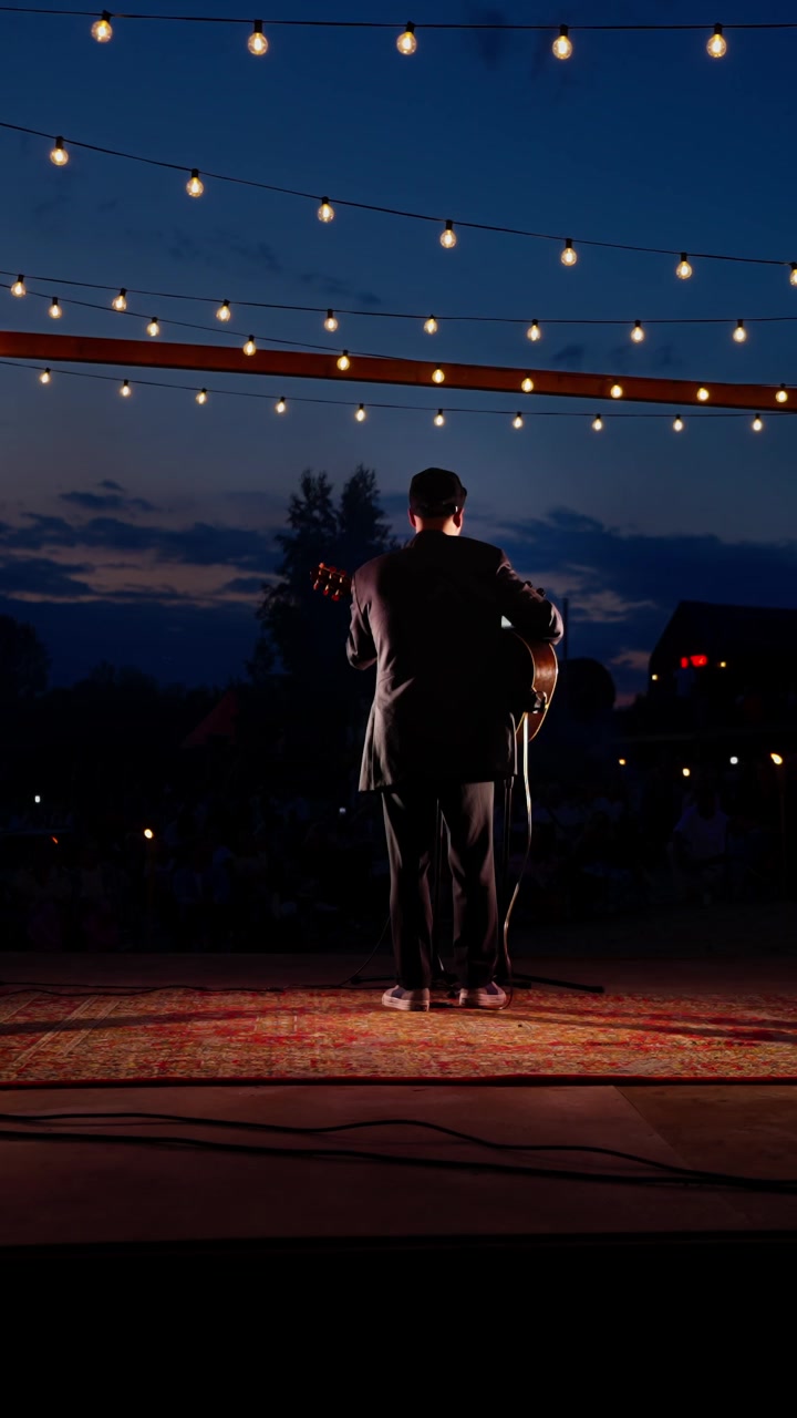 Musicista suona la chitarra acustica su un palco all'aperto al tramonto