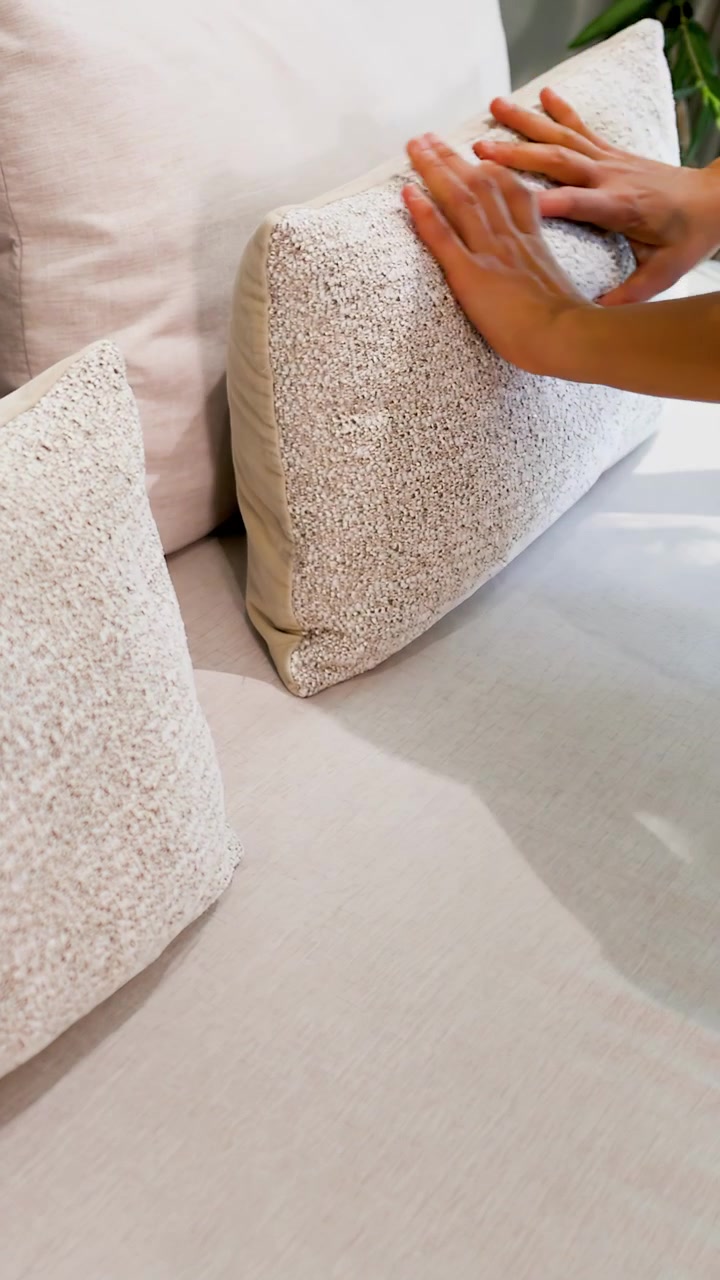 Le mani di una donna asiatica accarezzano un cuscino decorativo testurizzato su un divano del soggiorno di colore neutro.