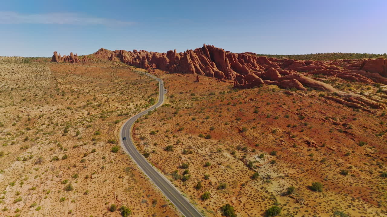 Dry desert with little greenery and road going through it. Beautiful canyons of Arches National park from aerial perspective.