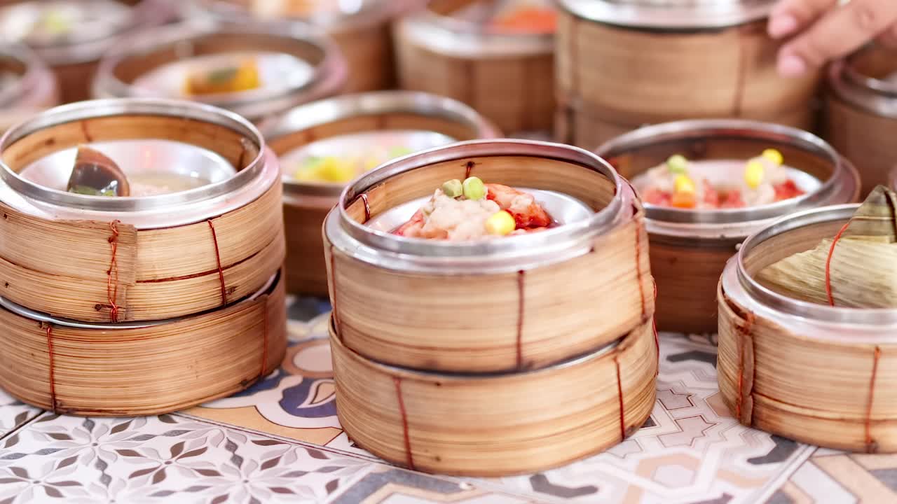 Close-up of hands picking dim sum from neatly arranged bamboo baskets on a patterned table.
