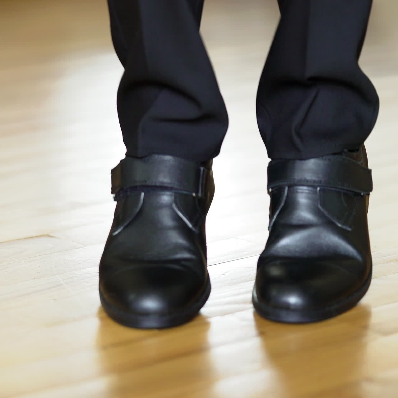 Man's legs with suit trousers and black leather shoes walking on the wooden floor. Young male walks on a spot and shows his new shoes.Close-up