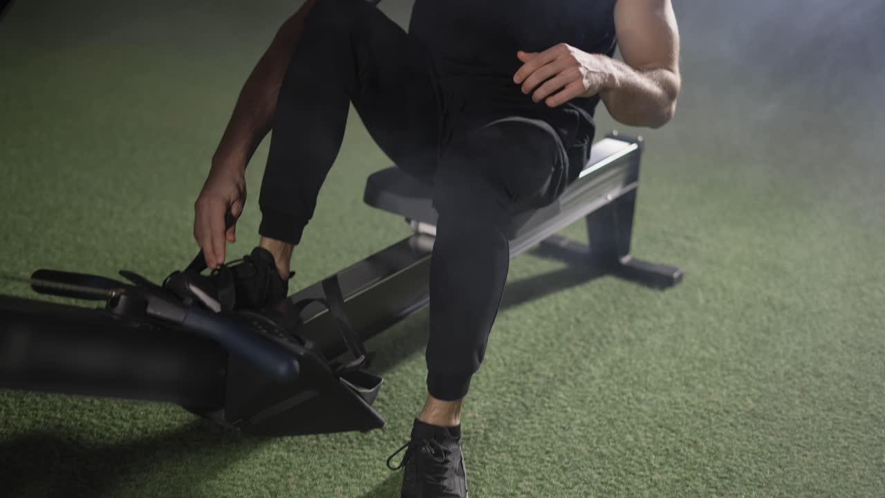 Bearded sportsman works out in gym with rowing machine, close up