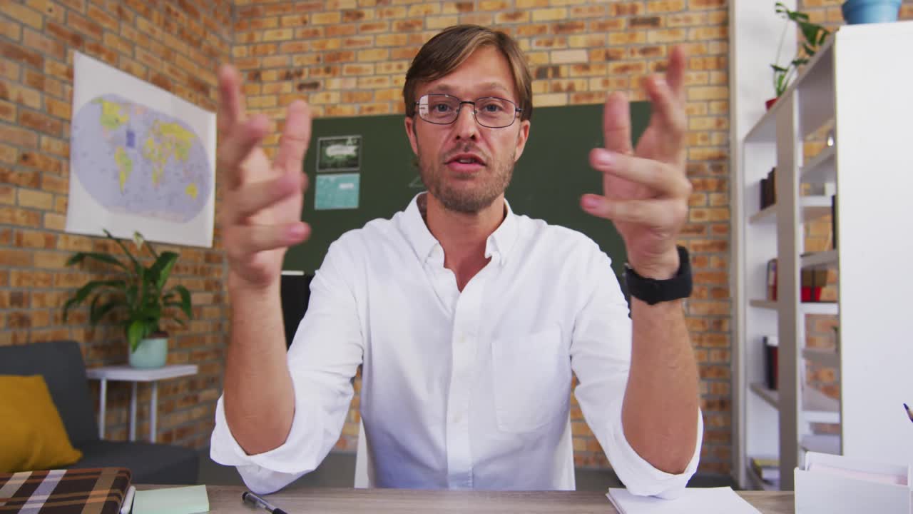 Portrait of caucasian male teacher teaching on videocall in the classroom at school