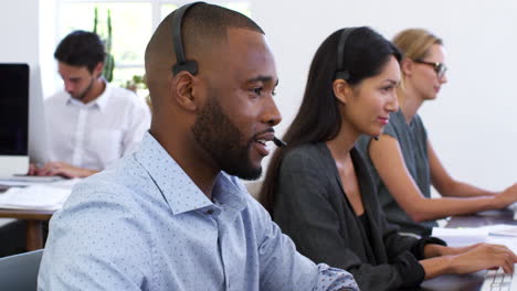 Un-Hombre-Negro-Con-Auriculares-Sonríe-A-La-Cámara-En-Una-Oficina-Abierta