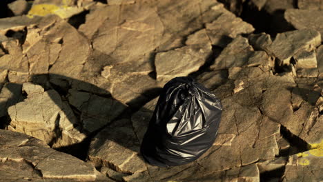 Bolsa-De-Basura-Negra-Yacía-En-Una-Playa-Rocosa