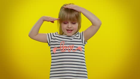 a young girl with blonde hair wearing a striped shirt with the word 'love' on it, smiling and posing in front of a yellow background.