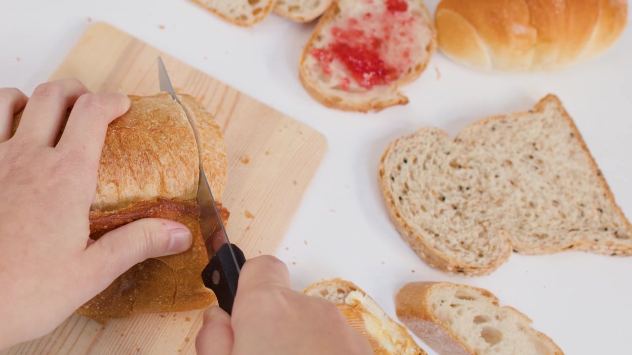 Overhead shot of hands using a serrated knife to slice crusty sourdough bread on wood.