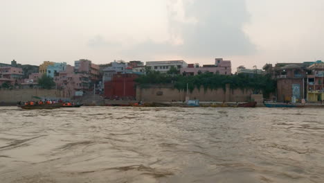 Cinemática-Río-Ganges-Chowk-Gente-En-Crucero-Canal-Barco-Varanasi-Norte-De-La-India-Estado-Antigua-Ciudad-Santa-Khidkiya-Ghat-Pradesh-Provincia-Paisaje-Gris-Nublado-Santo-Fangoso-Marrón-Seguir-Izquierda-Movimiento