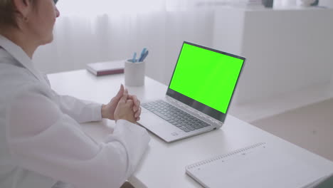 cita en línea con el médico mujer médico está mirando la pantalla verde de la computadora portátil para la tecnología de clave de croma comunicándose en línea por chat de video