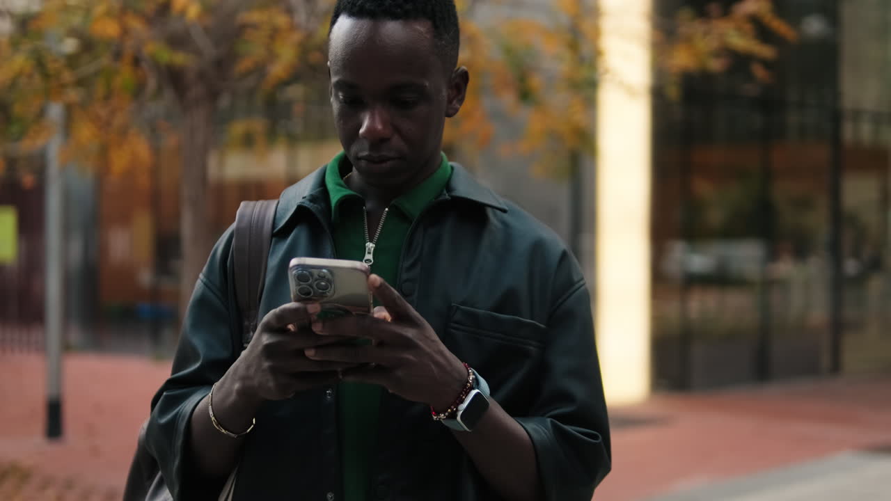 Young Black Man Typing on Smartphone Outdoors in City